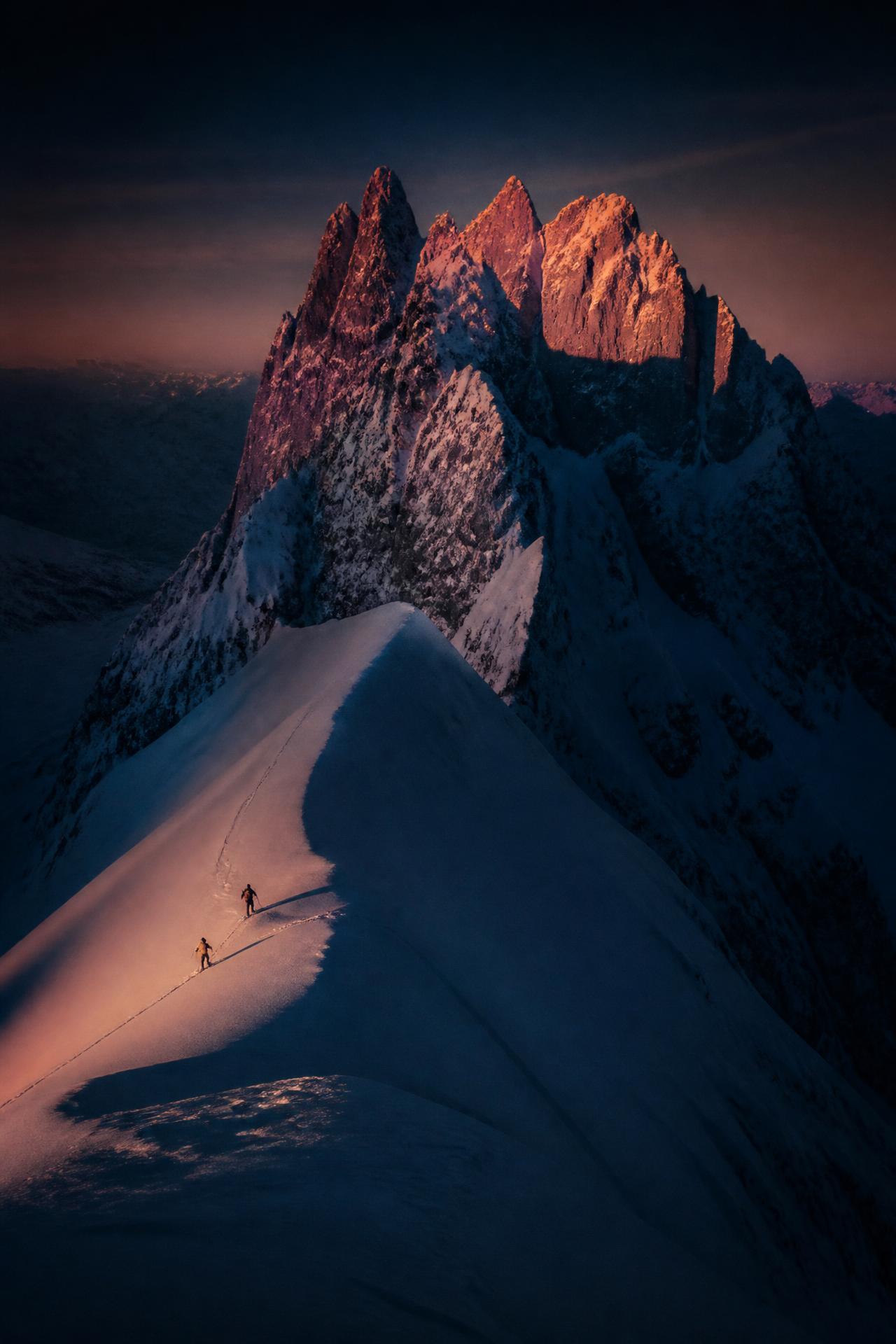 Sciatore in cresta all'alba con vette innevate illuminate di arancione